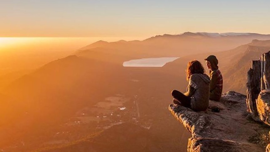 Two people perched on a rock overlooking valleys and ranges.