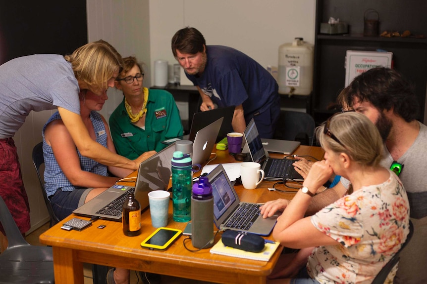 A group of people with laptops sit around a table.