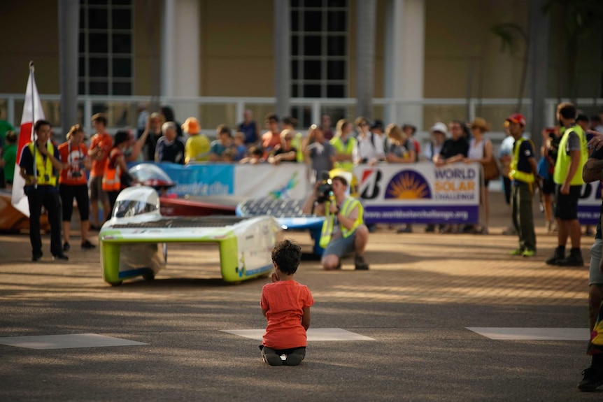 Crowds of people watching a solar car drive past.