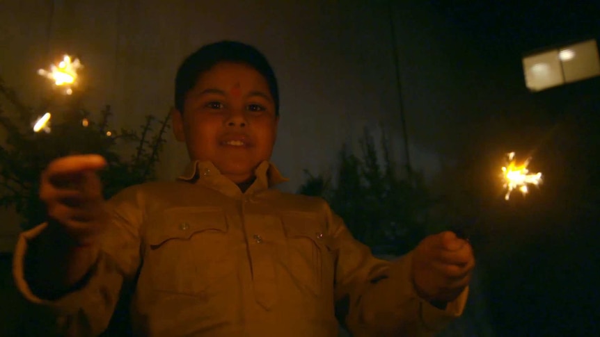 A boy holding up two sparklers at night