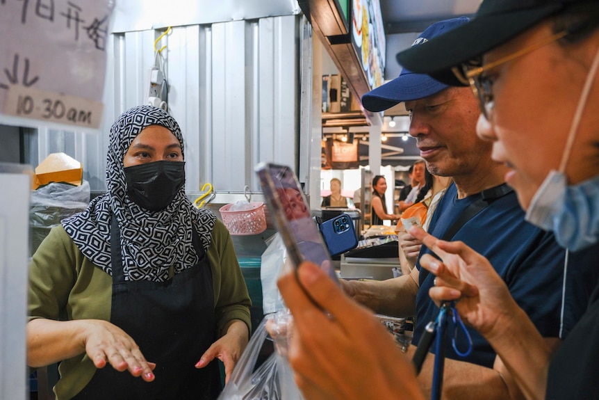 A woman talking to customers at a food stall. 