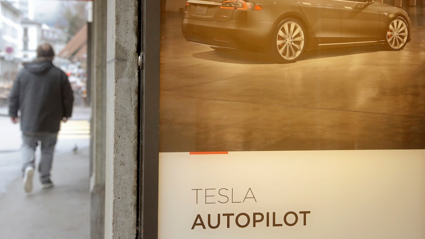 a man walks past a Tesla showroom advertising the Tesla Autopilot feature