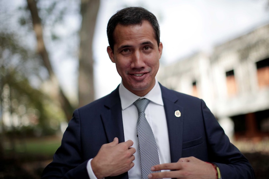 A man smirking while adjusting his navy blue suit jacket