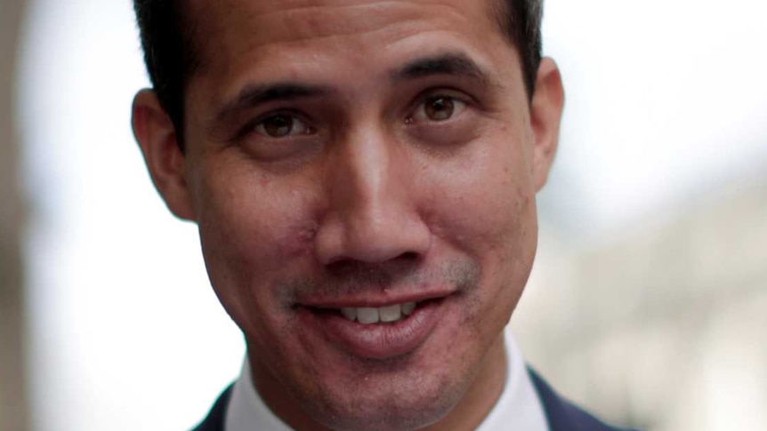 A man smirking while adjusting his navy blue suit jacket