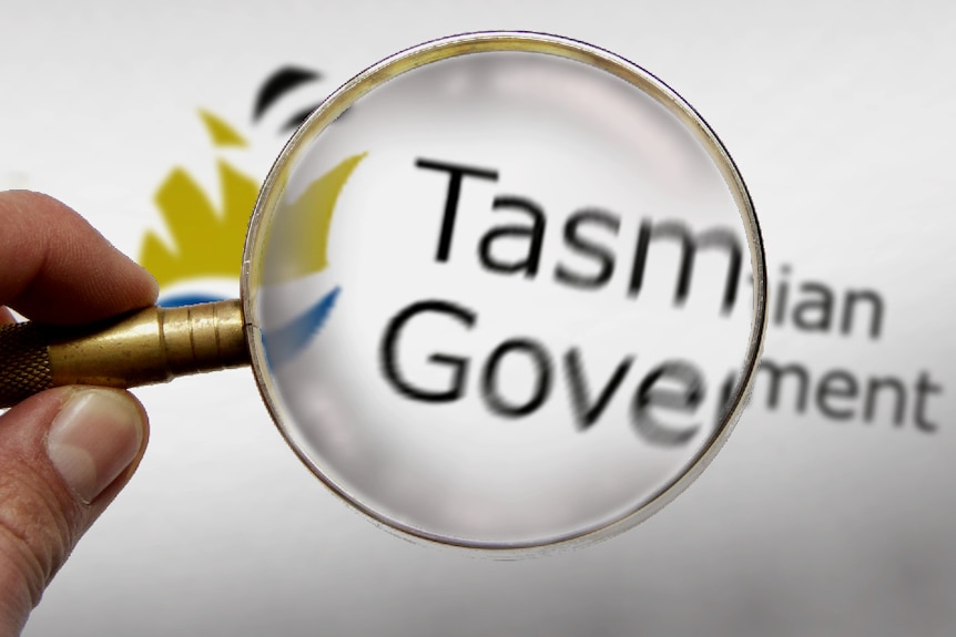 Hand holding a magnifying glass over Tasmanian Government letterhead.