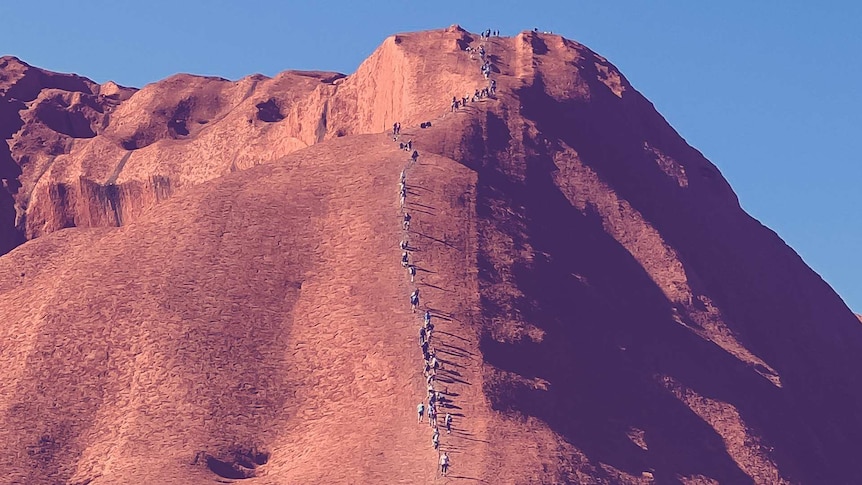 A section of Uluru that people can climb shows lots of people making the climb up the rock.