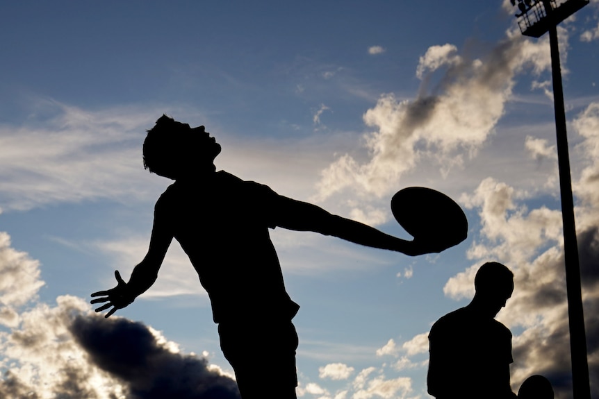 A silhouette of an Australian football umpire throwing the ball in from the boundary.