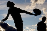 A silhouette of an Australian football umpire throwing the ball in from the boundary.