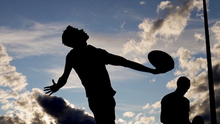 A silhouette of an Australian football umpire throwing the ball in from the boundary.