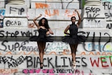 Two African American ballerinas standing on the base of a statue covered in graffiti
