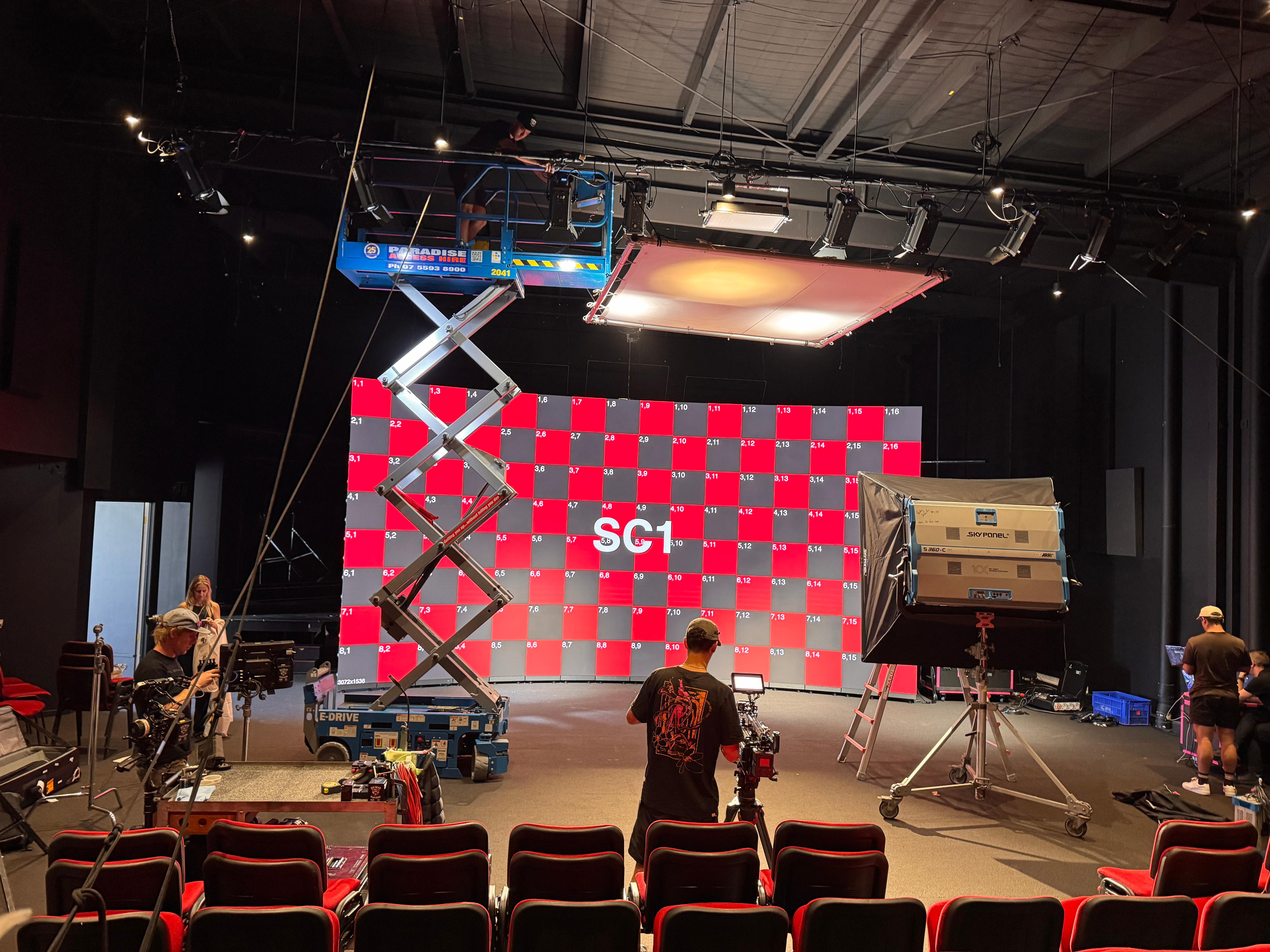 People working around a big screen with seating and lighting in front of it.