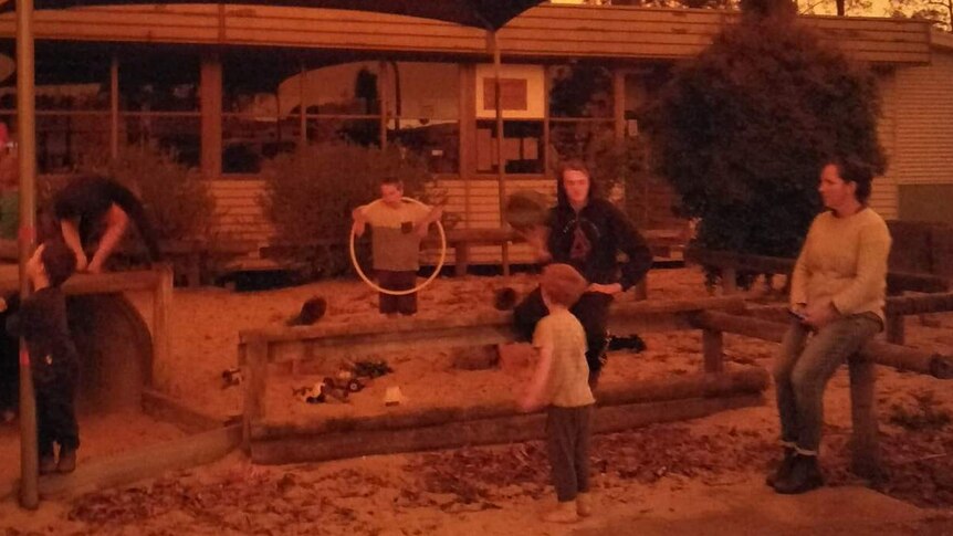 Parents and children in a playground where the sky is orange.