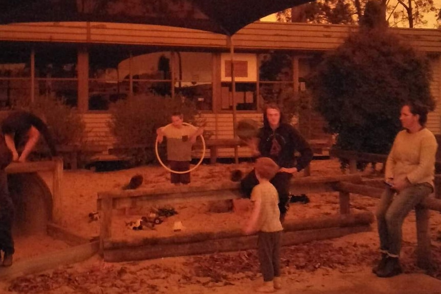 Parents and children in a playground where the sky is orange.