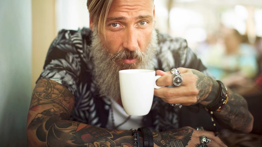 A bearded man sipping coffee looks into the camera
