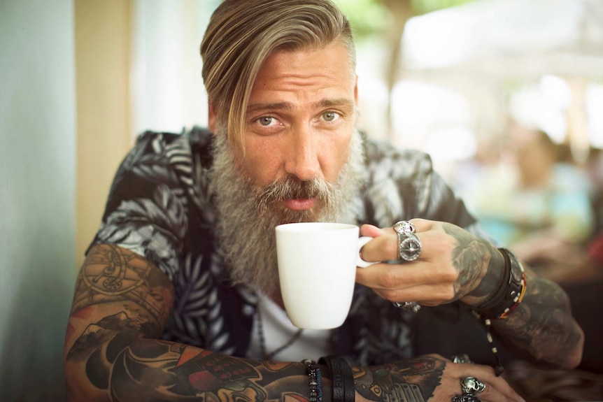 A bearded man sipping coffee looks into the camera