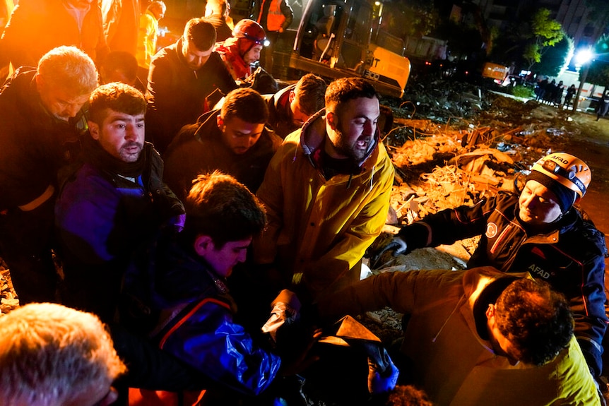 Emergency team members carry the body of a person found in the rubble of a destroyed building in Adana, Turkey.