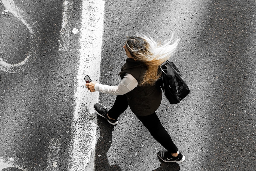 A woman crossing the street holding a phone.