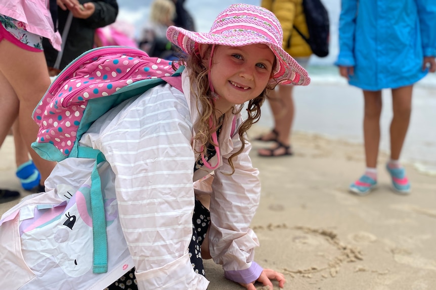 A little girl with a pink hat in a raincoat on the beach.