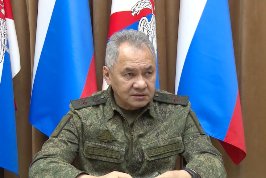 Close up of army general seated in front of Russian flags.