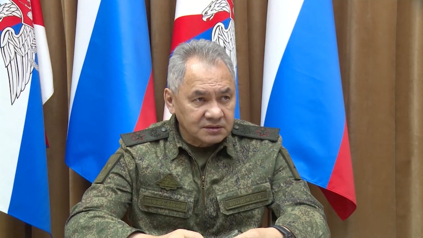 Close up of army general seated in front of Russian flags.