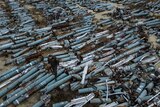 A man in Ukrainian army fatigues walks over a mass of blue metal cylinders lying in a scrapyard.