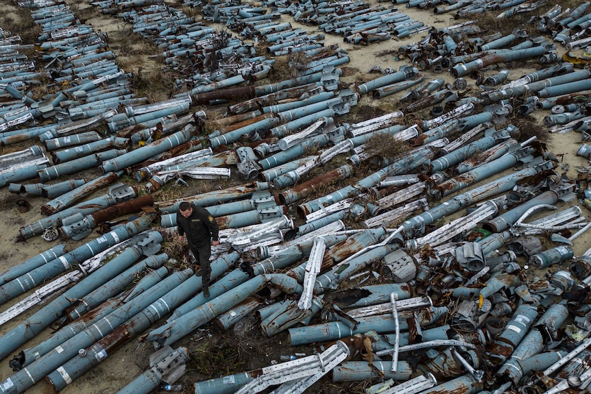A man walks over hundreds of collected parts of Russian rockets laying on the ground.