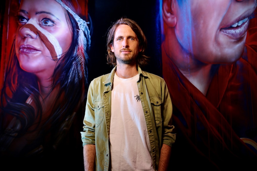 Artist Adnate stands in front of two murals he painted.