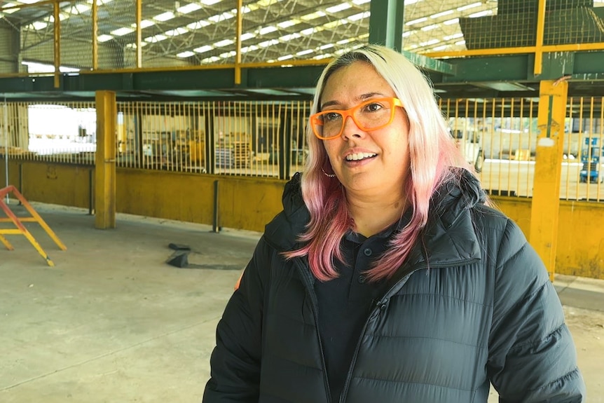 Woman with pink and white hair smiles in construction shed.