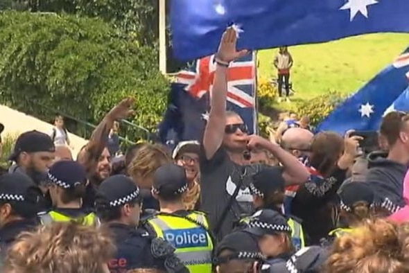 A man surrounded by Australian flags and police performs a Nazi salute