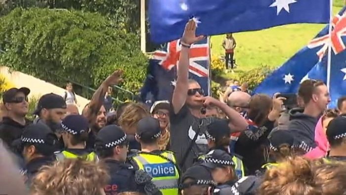 A man surrounded by Australian flags and police performs a Nazi salute