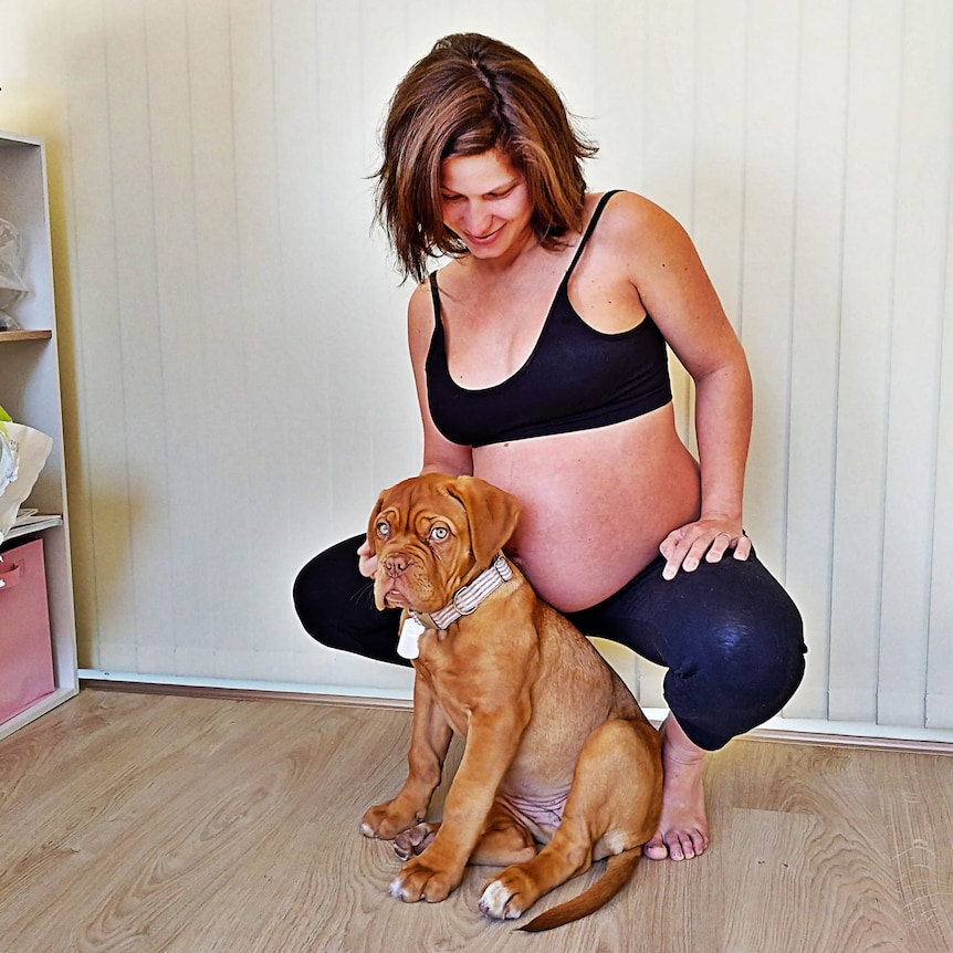 A heavily pregnant woman smiles down at a dog.