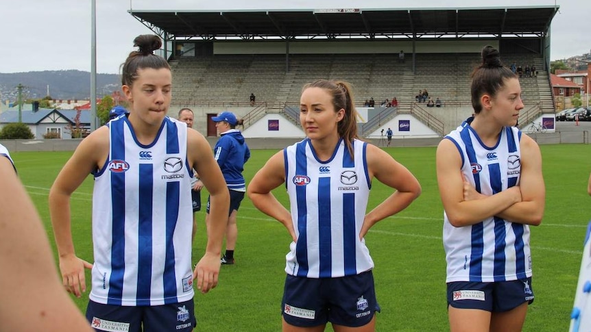 Three AFLW players stand in a row on the footy field.