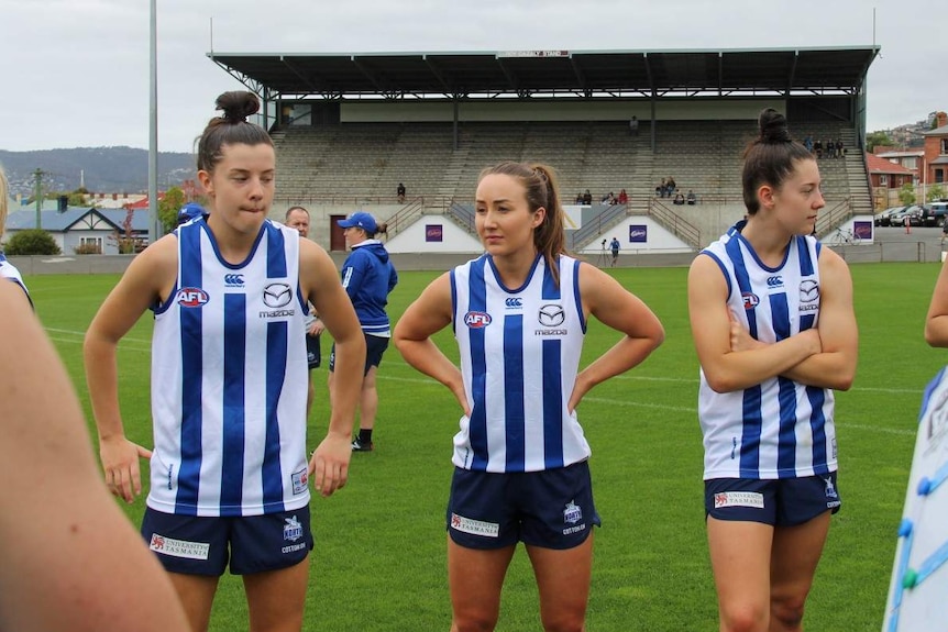 Three AFLW players stand in a row on the footy field.