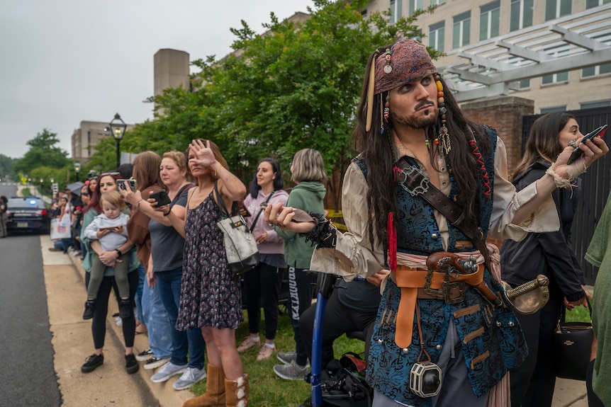 A group of people, including a man dressed as Jack Sparrow, line a road in the US