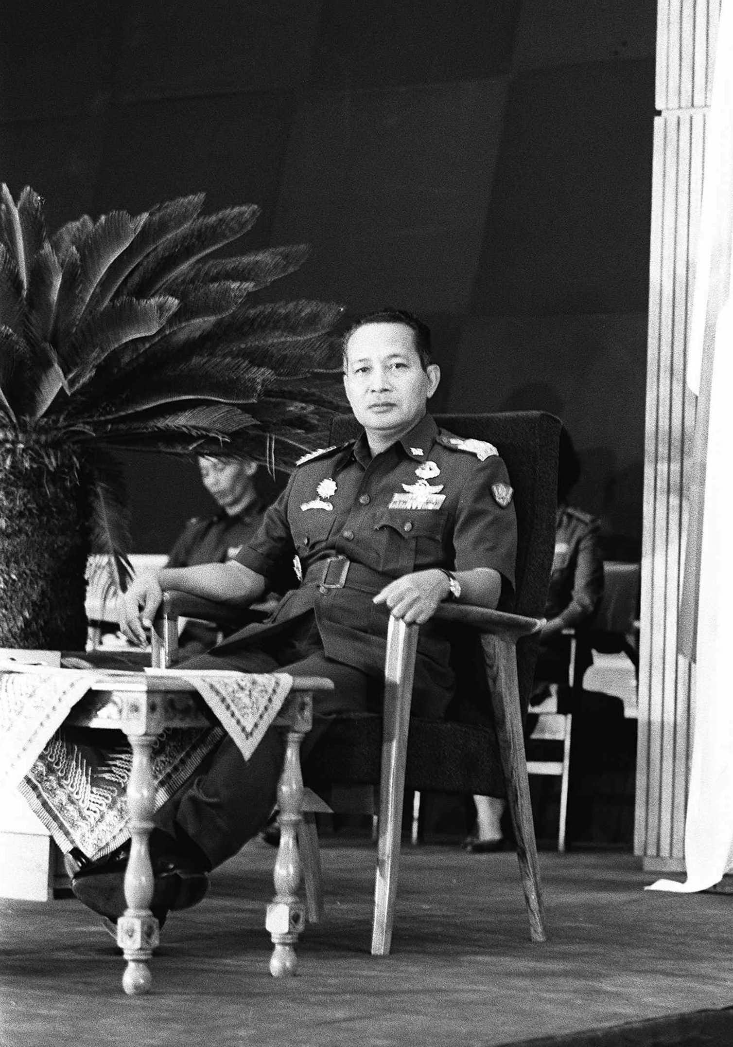 An Indonesian man in a military uniform poses for a photo from a basic armchair