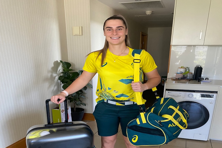 A woman in Australian uniform with a suitcase smiling inside a room.