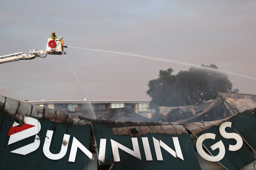 A firefighter atop a crane sprays water over a gutted Bunnings Warehouse in Inglewood with a big Bunnings logo visible.