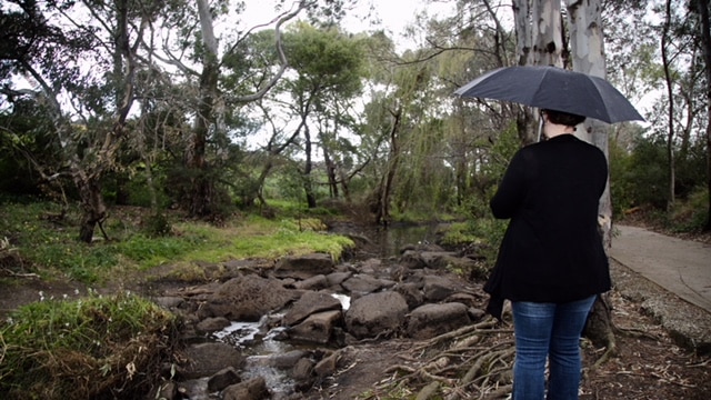 Woman stands holding umbrella next to creek with rocks