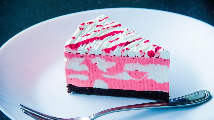 A piece of pink marbled cheesecake sits on a white plate next to a fork. 