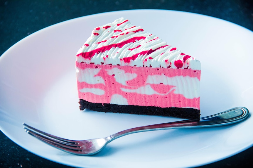 A piece of pink marbled cheesecake sits on a white plate next to a fork. 