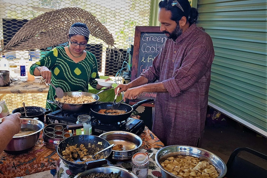 Woman wearing green dress giving a cooking workshop surrounded by full pots and pans