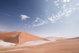 People and camels walk through the empty quarter desert in the middle east