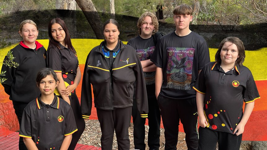 Seven smiling Indigenous people pose for a photo outdoors.