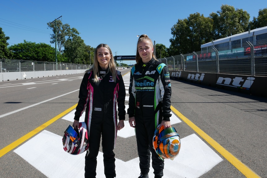 Deux femmes debout dans des combinaisons de course tenant des casques sur la piste de course.