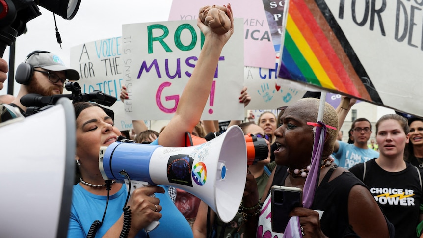 A woman holds a plastic foetus up in the air as another protester shouts at her. 