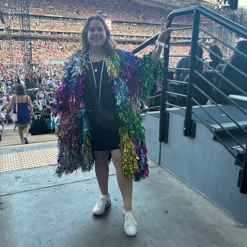 A woman in a sparkly coat stands inside a stadium.