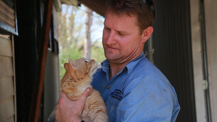 A man holds a ginger cat, which is staring up at him.