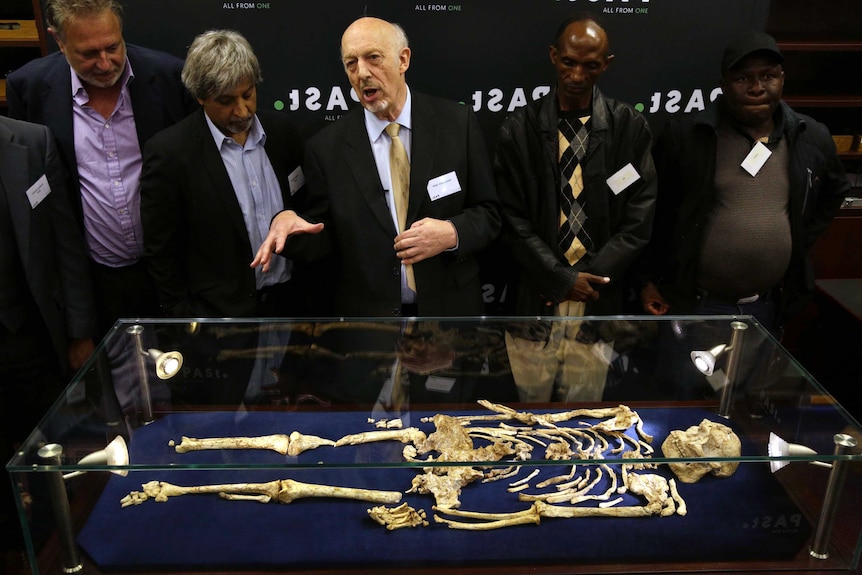 A man talks to a group while standing behind a display case holding a skeleton.