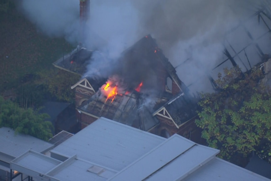 An aerial shot shows fire in the destroyed roof of a building.