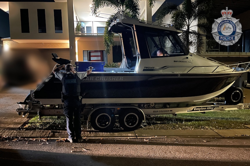 A boat on a suburban street in Darwin with an investigator inspecting the inside of the vessel.